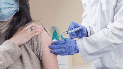 vrouw met mondmasker krijgt vaccinatie in linkerarm